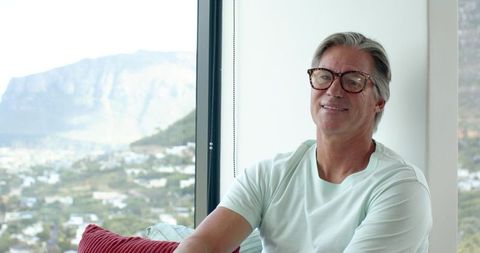 Senior man relaxing by window with mountain view wearing mint t-shirt and glasses