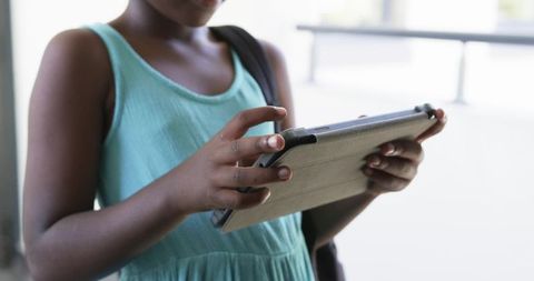 African teen holding tablet in folio wearing mint dress and backpack by railing