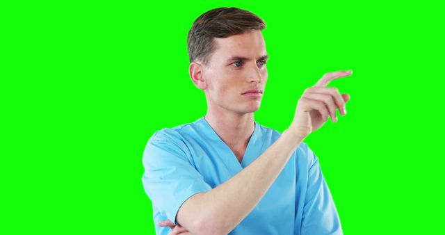 Male healthcare professional in blue scrubs is interacting with a virtual interface, set against a green screen background. This versatile and tech-savvy image is perfect for illustrating themes related to modern medical technology, telemedicine, digital healthcare, and futuristic healthcare innovations. It can be used in presentations, educational materials, health tech articles, and technology integration case studies.