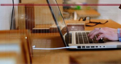 Hands typing on laptop with floating data overlay over warm wooden coworking workspace