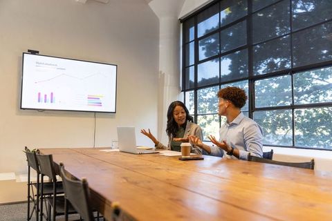 Diverse coworkers discussing analytics and strategy in modern boardroom, collaborating over laptop