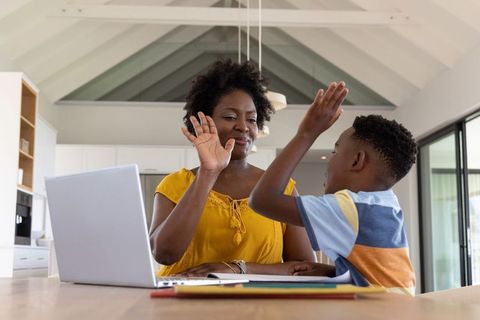 African american mother and son high-fiving while studying in bright modern kitchen