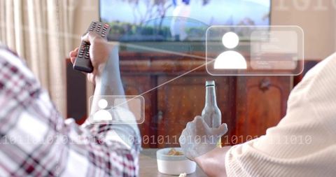 Two black men watching tv together holding remote and beer with snacks on table