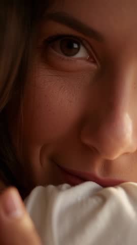 Vertical video of woman waking and hugging pillow, gentle smile and soft morning gaze