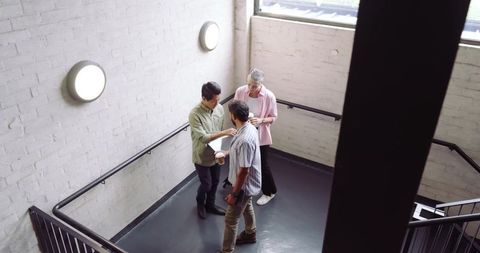 Diverse colleagues networking on office stairwell with coffee
