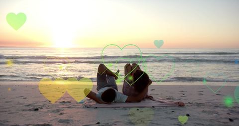 Romantic Couple Relaxing on Beach at Sunset with Floating Hearts