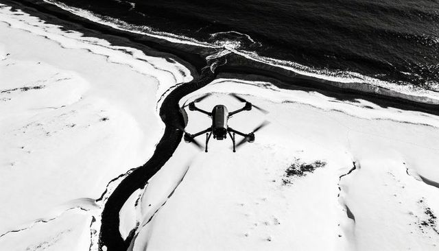 Quadcopter drone hovering over snowy coastline with winding dark river, winter aerial