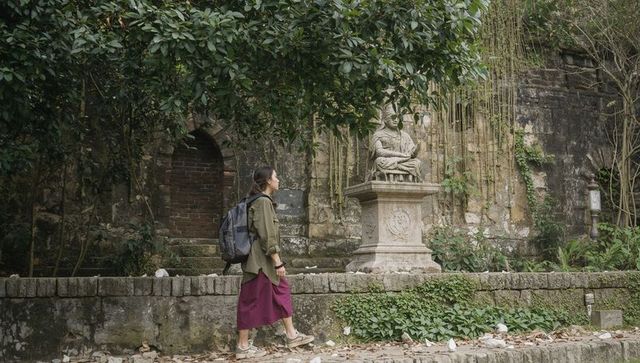 Solo traveler exploring historic garden wall and classical statue with backpack, vines