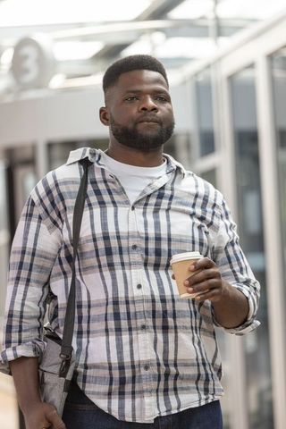 African american commuter holding coffee on train platform carrying gray shoulder bag