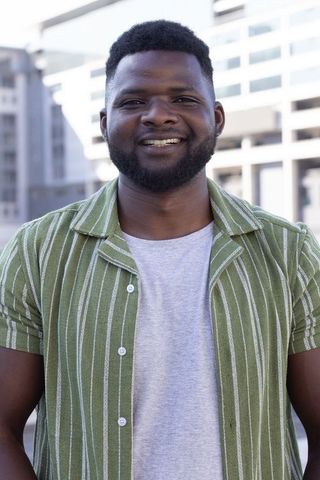 Smiling african man standing on rooftop wearing green striped shirt urban lifestyle portrait