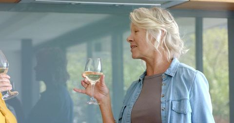 Mature women casual socializing toasting with white wine near large windows and greenery