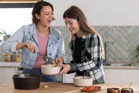 Friends cooking together in modern kitchen laughing while scraping batter into mixing bowl