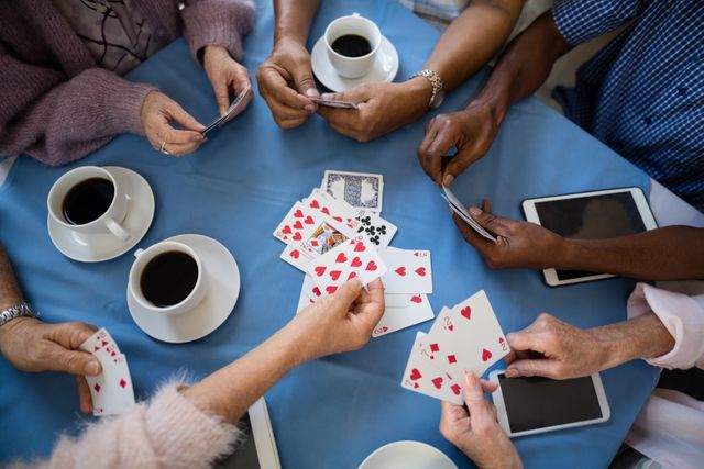 Senior individuals are gathered around a table, enjoying a card game and coffee. This scene highlights social interaction, leisure activities, and community among elderly people in a nursing home. Ideal for use in articles or advertisements about senior living, retirement communities, social activities for the elderly, and promoting active lifestyles for seniors.