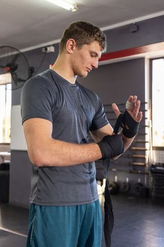 Male athlete wrapping hand wraps in gym preparing for boxing training, focused workout