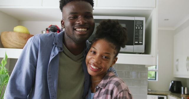 This image captures a tender moment of a smiling couple embracing in a modern kitchen. They are dressed in casual clothing, adding a touch of everyday life and warmth. Perfect for themes centered on love, romance, happy home life, intimacy, and genuine emotional connections. Ideal for use in advertisements, blogs about relationships, home and lifestyle magazines, or sociocultural studies.