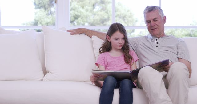 Grandfather Reading Book to Granddaughter on White Couch by Window - Download Free Stock Images Pikwizard.com