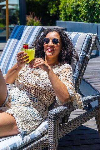 African american woman relaxing poolside in crochet cover-up sipping tropical cocktail