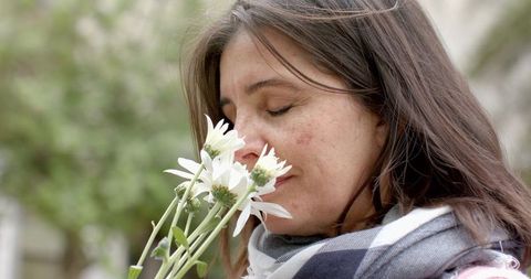 Mature woman smelling white daisies in park wearing plaid scarf, serene close-up