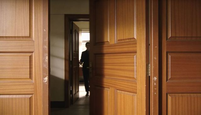 Backlit silhouette of businessman standing in corridor framed by wooden paneled doors