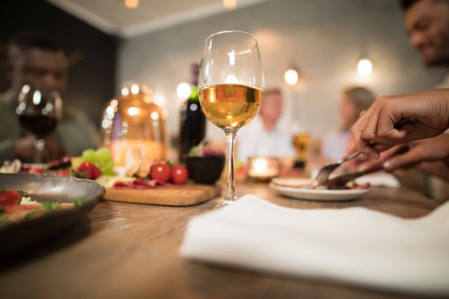 Glass of white wine on a dining table in a restaurant with blurred people in the background. Ideal for use in articles or advertisements about dining experiences, social gatherings, restaurants, and gourmet cuisine.