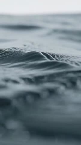 Vertical macro video of calm ocean surface capturing ripples, droplets and soft horizon