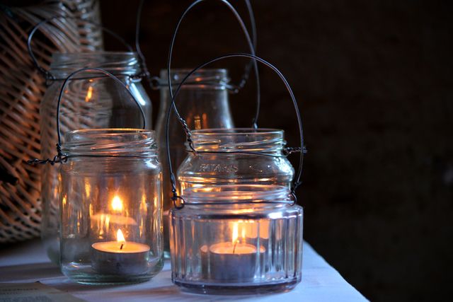 Rustic decor with glowing candles inside clear glass jars, creating a warm and calming ambiance. Perfect for themes related to relaxation, cozy interiors, rustic settings, evening relaxation, and home decor ideas. Ideal for use in blog posts, social media graphics, home decor magazines, and advertisements for candles or rustic home accessories.