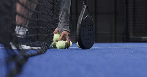 Man Picking Padel Balls on Blue Court Modern Game Scene