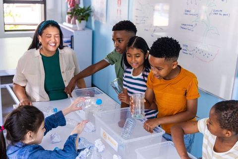 Elementary students and female teacher sorting plastic bottles for school recycling lesson