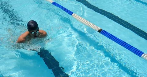 Competitive swimmer powering breaststroke through sunlit outdoor lap pool with lane divider