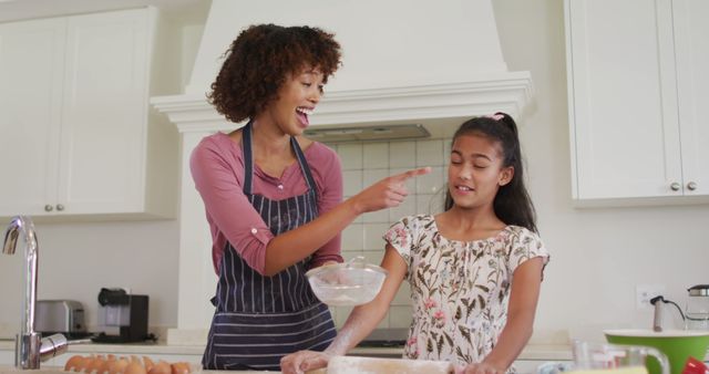 This joyful depiction of an African American mother and daughter engaging in a baking activity in their home kitchen can be useful for various contexts. It is ideal for adding warmth and authenticity to family-related content, cooking blogs, advertisements for kitchenware, parenting articles, and commercials focusing on family love and togetherness. The image reflects modern domestic life, highlighting themes such as bonding, joy, and shared experiences.