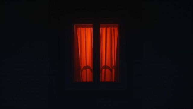Mystical glowing window with red-orange curtains at night