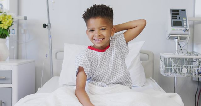 Portrait of happy african american boy patient sitting up in bed at hospital smiling. Medicine, healthcare, lifestyle and hospital concept.