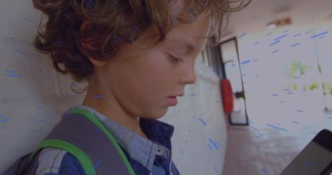 Leaning Child Checking Handheld Device in School Corridor With Backpack and Daylight