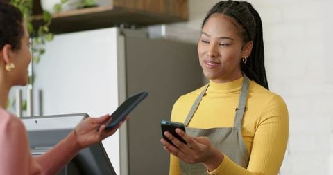 African american cashier accepting contactless mobile payment with card reader in cafe