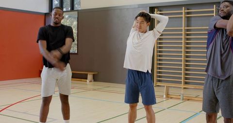 Diverse men warming up stretching chest and triceps in gymnasium before group workout