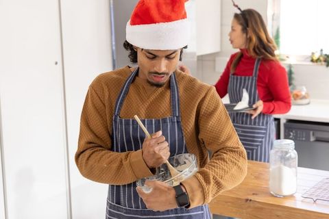 Diverse couple baking together in festive kitchen mixing batter wearing santa hat