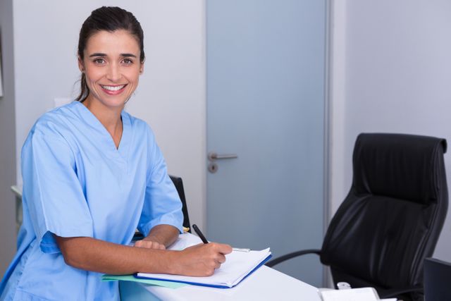 Portrait of doctor writing in file while sitting by table in clinic