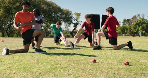 Diverse male athletes warming up with lunges on sunny cricket field before practice