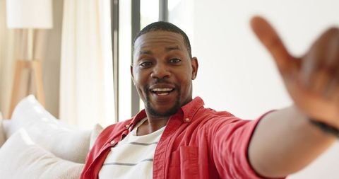 Smiling african american man reaching out while relaxing on couch in bright modern living room