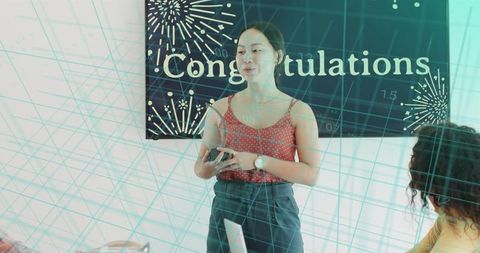 Woman presenting at office celebration holding smartphone with congratulations banner and teal grid