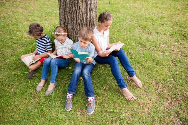 Children sitting under a tree in a park, reading books on a sunny day. Ideal for educational content, children's literature promotions, outdoor activities, and summer learning programs.