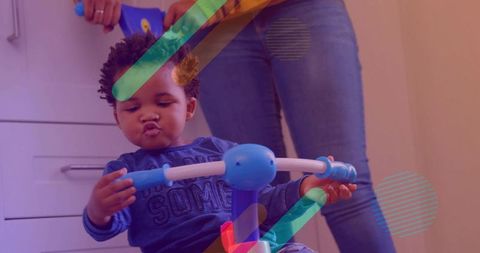 Toddler puckering and gripping ride-on handle during indoor play while caregiver guiding