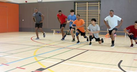 Multicultural male team performing agility drills and warm-ups on indoor gym hardwood court