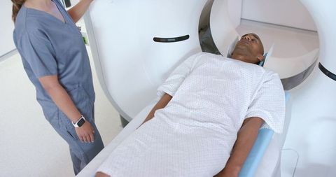 Male patient undergoing ct scan while technologist operating scanner in radiology suite