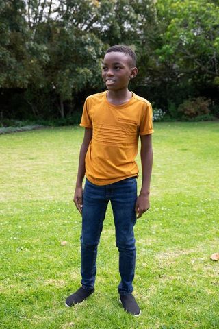 Afro-american boy in mustard t-shirt on lawn, in casual and relaxed outdoor setting