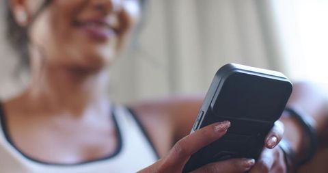 Woman reclining on couch using smartphone and earbuds, cozy home relaxation moment