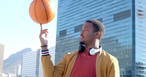 African american man spinning basketball on finger in urban plaza with glass skyline