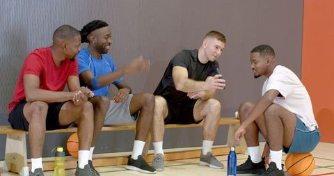 Multiracial men sharing basketball clip and cheering on bench during court break