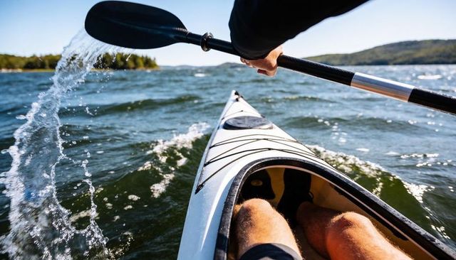 Male kayaker paddling through choppy lake waves splashing paddle bow view