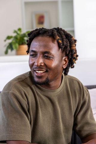 African american man smiling and relaxing on sofa in modern living room with plant and art